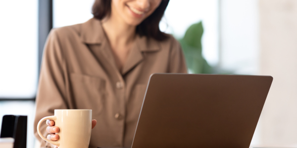 Mujer relajada frente a su portátil con una taza, utilizando recursos espirituales online para su bienestar diario.