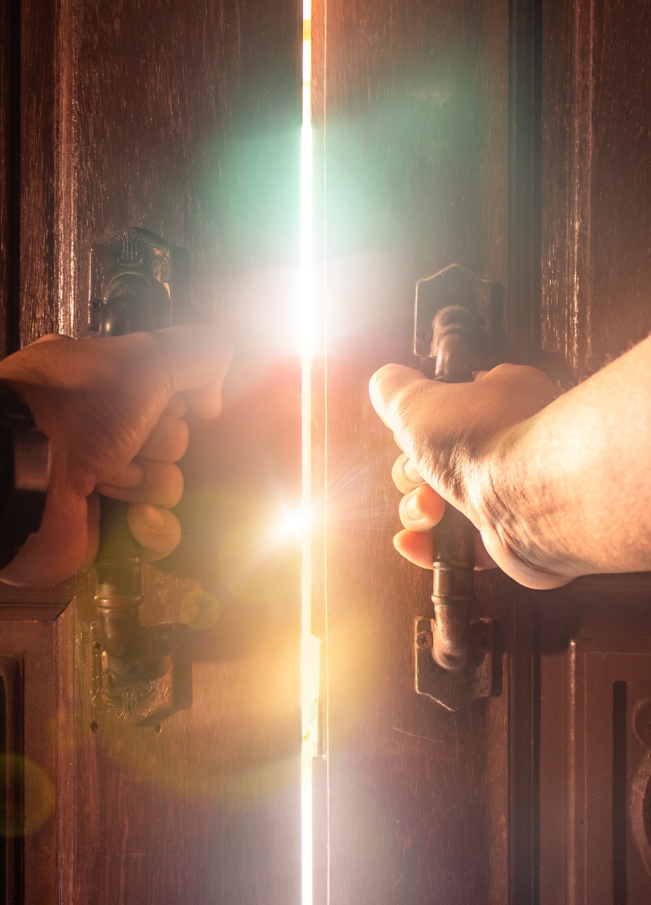 Manos masculinas abriendo una puerta desde la oscuridad hacia una luz intensa, simbolizando el inicio de la membresía espiritual Puerta de Luz