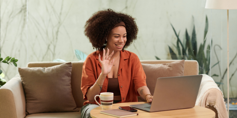 we-prepare-together-online-energy-healer-for-parties-phoenix Woman in earth-tone clothing talking on a laptop while drinking tea, with a phone and notebook beside her, preparing an online energy healing session